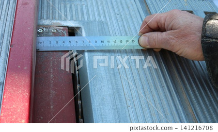 the hand of a craftsman using a metal ruler to measure the distance from the rip fence to the saw blade on a circular saw for precise adjustment before making a cut. the hand of a craftsman using a metal ruler to measure the distance from the rip fence to the saw blade on a circular saw for precise adjustment before making a cut. 141216708