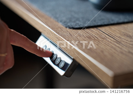 Finger pressing control button on adjustable wooden desk to change desk height Finger pressing control button on adjustable wooden desk to change desk height 141216756