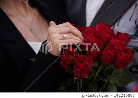 Close up of woman hand wearing engagement ring holding a bouquet of red roses in black formal attire Close up of woman hand wearing engagement ring holding a bouquet of red roses in black formal attire 141216898