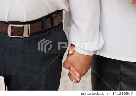 Close up of a man and woman holding hands wearing formal white shirts and dark trousers and skirt. Close up of a man and woman holding hands wearing formal white shirts and dark trousers and skirt. 141216907