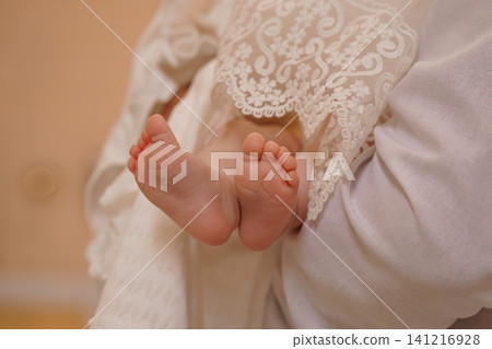 Close up of newborn baby feet in white lace christening gown against a soft neutral background. Close up of newborn baby feet in white lace christening gown against a soft neutral background. 141216928