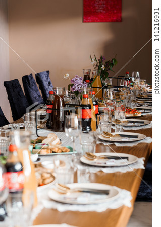 Long wooden dining table set with plates, glasses, and soft drinks for a group celebratory meal indoors. Long wooden dining table set with plates, glasses, and soft drinks for a group celebratory meal indoors. 141216931