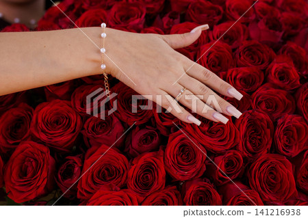 Elegant female hand with pearl bracelet and gold ring resting on a bed of deep red roses. Elegant female hand with pearl bracelet and gold ring resting on a bed of deep red roses. 141216938