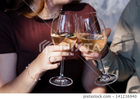 Couple Clinking White Wine Glasses During Outdoor Celebration in Soft Natural Sunlight Couple Clinking White Wine Glasses During Outdoor Celebration in Soft Natural Sunlight 141216940