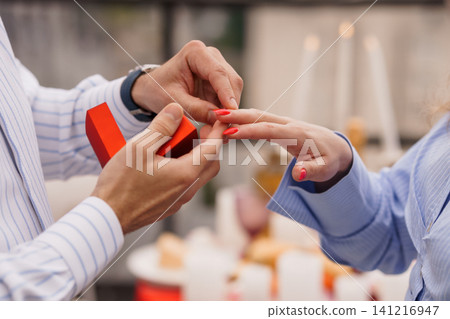 Man Proposing to Woman with Ring in Red Box During Romantic Dinner with Candles and Soft Lighting Man Proposing to Woman with Ring in Red Box During Romantic Dinner with Candles and Soft Lighting 141216947