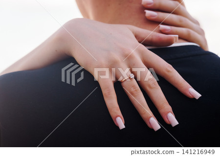 Woman hugging man from behind wearing diamond engagement ring on finger with black suit background Woman hugging man from behind wearing diamond engagement ring on finger with black suit background 141216949