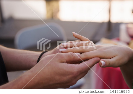 Man holding woman hand with diamond engagement ring during outdoor wedding ceremony in soft natural light. Man holding woman hand with diamond engagement ring during outdoor wedding ceremony in soft natural light. 141216955