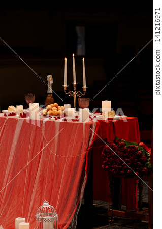 Romantic dinner for two with red tablecloth, candles, champagne, and red roses in a dark moody setting. Romantic dinner for two with red tablecloth, candles, champagne, and red roses in a dark moody setting. 141216971