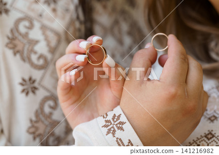 Woman holding two gold wedding bands in hands wearing traditional embroidered folk clothing. Woman holding two gold wedding bands in hands wearing traditional embroidered folk clothing. 141216982