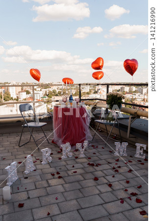 Romantic Marriage Proposal Setup on City Rooftop with Red Heart Balloons and Marry Me Letters at Sunset. Romantic Marriage Proposal Setup on City Rooftop with Red Heart Balloons and Marry Me Letters at Sunset. 141216990