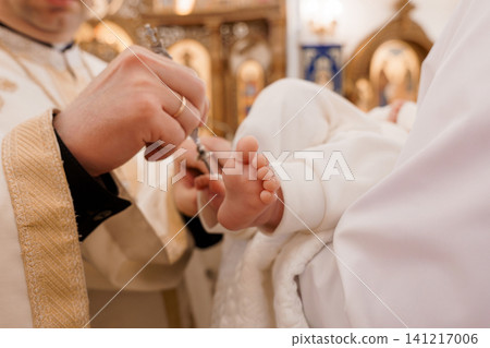 Orthodox priest performing baptism ritual on infant feet inside golden church interior Orthodox priest performing baptism ritual on infant feet inside golden church interior 141217006