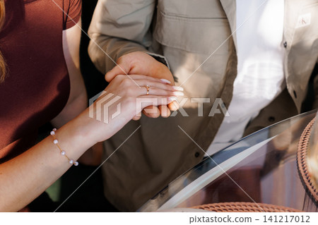 Close up of couple holding hands with gold engagement ring and pearl bracelet in warm natural lighting. Close up of couple holding hands with gold engagement ring and pearl bracelet in warm natural lighting. 141217012