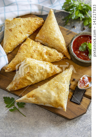 Traditional asian food. Vegetarian samsa (samosa) stuffed with potato with tomato sauce on a stone surface. Healthy breakfast, snack. Copy space. Traditional asian food. Vegetarian samsa (samosa) stuffed with potato with tomato sauce on a stone surface. Healthy breakfast, snack. Copy space. 141217833
