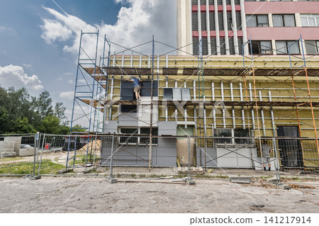 Workers are installing mineral wool insulation on the building's facade using scaffolding. The sky is clear and the construction site is active Workers are installing mineral wool insulation on the building's facade using scaffolding. The sky is clear and the construction site is active 141217914