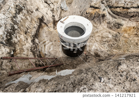 Workers are building a concrete sewer well in a deep pit at a construction site. Tools and a ladder are present near the well during daytime Workers are building a concrete sewer well in a deep pit at a construction site. Tools and a ladder are present near the well during daytime 141217921