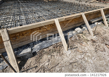Workers place steel reinforcement bars into position for a concrete pour. The site is under construction with materials ready for the pour Workers place steel reinforcement bars into position for a concrete pour. The site is under construction with materials ready for the pour 141217926