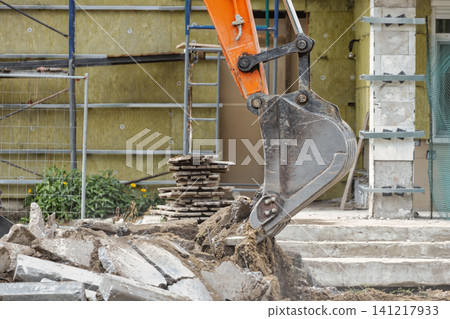 An excavator digs into the ground, moving soil and debris at a construction site. Workers prepare for new structures in a developing area An excavator digs into the ground, moving soil and debris at a construction site. Workers prepare for new structures in a developing area 141217933