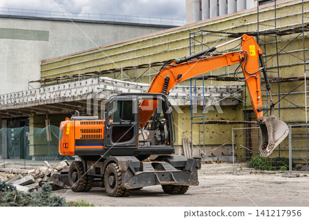 Excavator is at work on a construction site moving dirt and debris as workers prepare area for new structure near existing buildings in city Excavator is at work on a construction site moving dirt and debris as workers prepare area for new structure near existing buildings in city 141217956