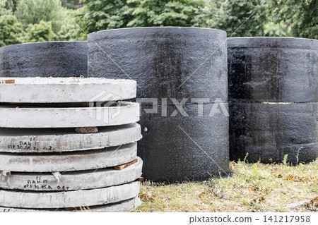 Workers place round black and gray concrete structures in a grassy area. The scene shows trees and an overcast sky. Tools are scattered nearby as work continues Workers place round black and gray concrete structures in a grassy area. The scene shows trees and an overcast sky. Tools are scattered nearby as work continues 141217958