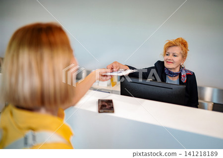 Customer checking in at reception desk passing documents to employee Customer checking in at reception desk passing documents to employee 141218189