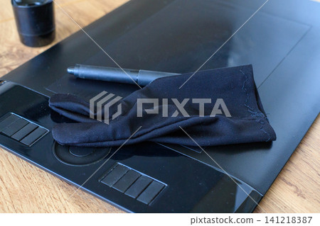 Black two-finger artist glove and digital pen stylus lying on graphic drawing tablet, creative retoucher workspace background 141218387