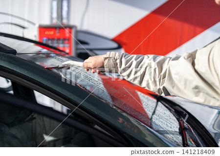 Person cleaning and wiping back window of a vehicle with water squeegee tool at manual car wash. Person cleaning and wiping back window of a vehicle with water squeegee tool at manual car wash. 141218409