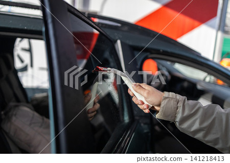 Person cleaning and wiping back window of a vehicle with water squeegee tool at manual car wash. Person cleaning and wiping back window of a vehicle with water squeegee tool at manual car wash. 141218413