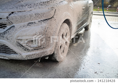 Young guy cleaning vehicle with pressure washer jet spray at manual car wash station. Young guy cleaning vehicle with pressure washer jet spray at manual car wash station. 141218428
