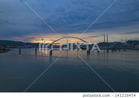 An aerial photograph taken at dawn in Shunan City, Yamaguchi Prefecture, capturing the Shunan Bridge and the surrounding industrial area. An aerial photograph taken at dawn in Shunan City, Yamaguchi Prefecture, capturing the Shunan Bridge and the surrounding industrial area. 141218454