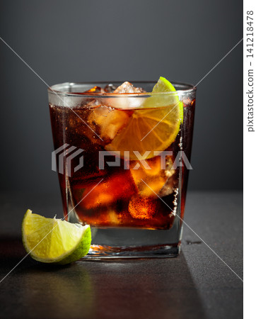 Refreshing cocktail with lime, cola and ice in a glass on a black table. Refreshing cocktail with lime, cola and ice in a glass on a black table. 141218478