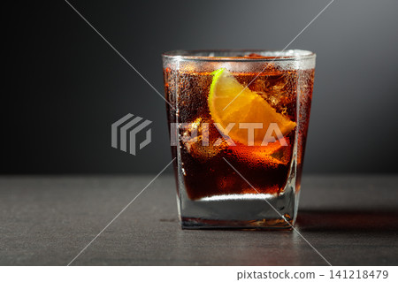 Refreshing cocktail with lime, cola and ice in a glass on a black table. Refreshing cocktail with lime, cola and ice in a glass on a black table. 141218479