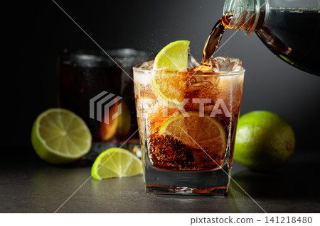 Refreshing cocktail with lime, cola and ice in a glass on a black table. 141218480