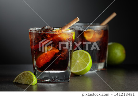 Refreshing cocktail with lime, cola and ice in a glass on a black table. Refreshing cocktail with lime, cola and ice in a glass on a black table. 141218481