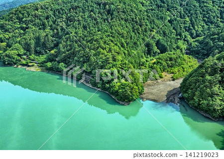 An aerial photograph overlooking the emerald green surface of Lake Ikawa in Shizuoka Prefecture and the surrounding lush green mountains and forests. An aerial photograph overlooking the emerald green surface of Lake Ikawa in Shizuoka Prefecture and the surrounding lush green mountains and forests. 141219023