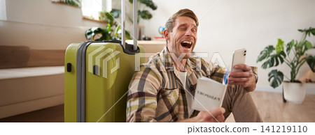 Happy man with suitcase, holding passport and using smartphone, going on holiday Happy man with suitcase, holding passport and using smartphone, going on holiday 141219110