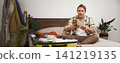 Portrait of man with suitcase, sitting and packing things for holiday, checking list of items for vacation, writing down, making notes in notebook 141219135