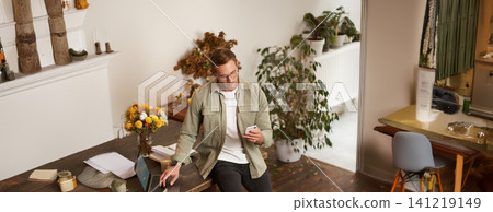 Portrait of a man in office, businessman making a phone call, having a conversation over the phone, receive a call, standing in office, leaning on table Portrait of a man in office, businessman making a phone call, having a conversation over the phone, receive a call, standing in office, leaning on table 141219149