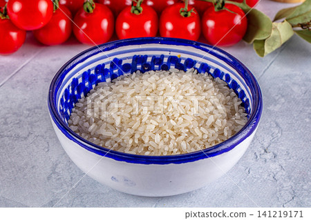 Bowl of uncooked rice with cherry tomatoes and bay leaves on stone surface Bowl of uncooked rice with cherry tomatoes and bay leaves on stone surface 141219171