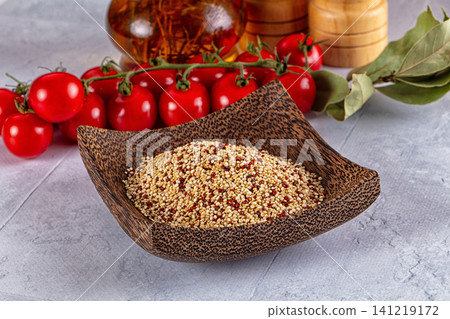 Quinoa in wooden bowl with cherry tomatoes and bay leaves on stone surface 141219172