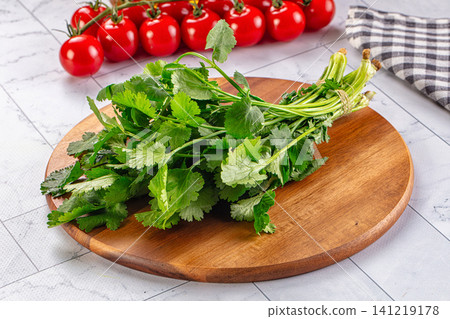 Fresh cilantro on wooden cutting board with cherry tomatoes background Fresh cilantro on wooden cutting board with cherry tomatoes background 141219178