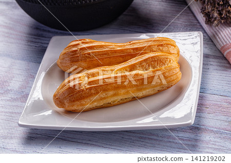 Two golden eclairs on white plate with rustic wood background 141219202