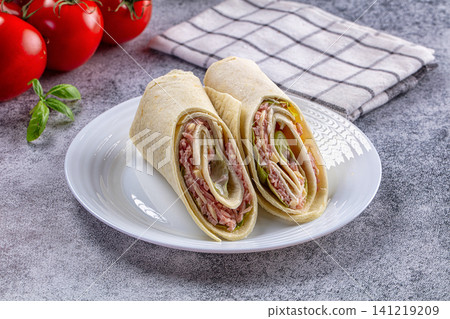 Wrapped sandwich with ham cheese and greens on white plate Wrapped sandwich with ham cheese and greens on white plate 141219209