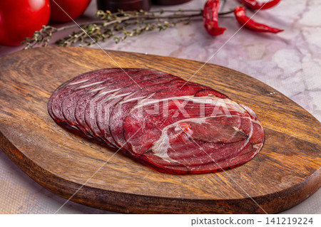 Sliced cured meat on wooden cutting board with red peppers and herbs Sliced cured meat on wooden cutting board with red peppers and herbs 141219224