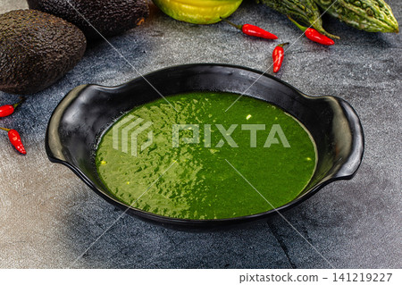 Green spinach cream soup in black ceramic bowl with avocado and chili peppers on dark stone background 141219227