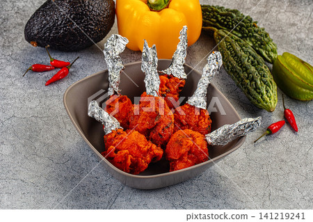 Spicy fried chicken wings with foil wrapped bones surrounded by fresh vegetables on textured gray surface 141219241