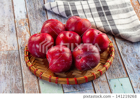Fresh red plums in woven basket on rustic wooden table Fresh red plums in woven basket on rustic wooden table 141219268