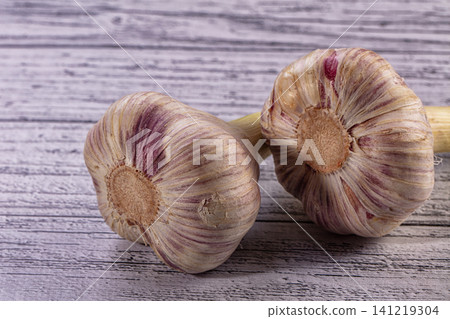 Two fresh garlic bulbs with purple stripes on a rustic wooden table Two fresh garlic bulbs with purple stripes on a rustic wooden table 141219304