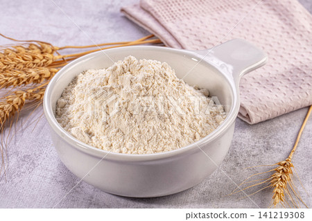 White ceramic bowl filled with fine wheat flour beside golden wheat stalks on textured surface White ceramic bowl filled with fine wheat flour beside golden wheat stalks on textured surface 141219308