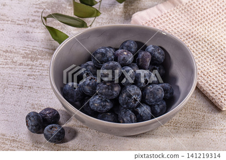 Fresh blueberries in gray ceramic bowl on textured surface with green leaves Fresh blueberries in gray ceramic bowl on textured surface with green leaves 141219314