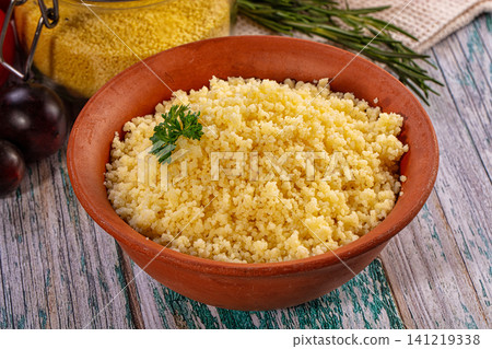 Couscous in terracotta bowl with parsley garnish on rustic wooden table Couscous in terracotta bowl with parsley garnish on rustic wooden table 141219338